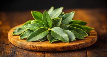 A bunch of green leaves are on a wooden cutting board. The leaves are fresh and appear to be from a tree photo