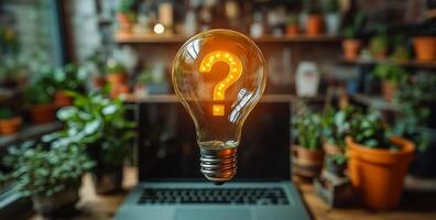 A light bulb with a question mark on it is floating above a laptop computer. Concept of curiosity and wonder, as if the light bulb is asking a question or seeking an answer photo