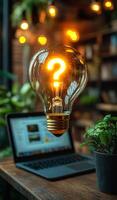 A light bulb with a question mark on it is lit up and placed on a table next to a laptop. Concept of curiosity and wonder photo