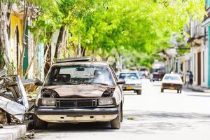 Old car resting on a tranquil street in Cuba amidst faded colors and lush greenery reflecting the charm of a bygone era photo
