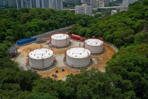 Overview of oil and gas refinery storage tanks nestled within a forested area in an urban landscape photo