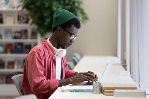 Successful African American guy programmer is typing code in laptop sits in office of IT company photo
