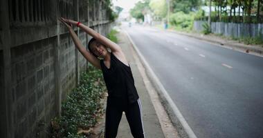 Young woman in sportswear and wireless headphones listening to music while stretching to warm up before. video