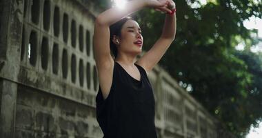 Handheld low angle view shot, Young woman in sportswear and wireless headphones listening to music while stretching to warm up before an outdoor workout on a sidewalk. video