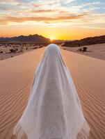 Person in white robe walking towards sunset in desert photo