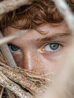 Close up portrait of a freckled redhead boy hiding behind branches photo