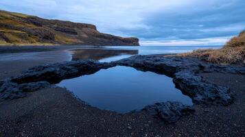 Tide pool on a black sand beach with cliffs in the background photo