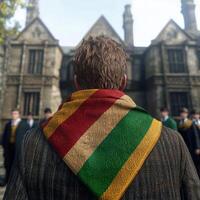 Student standing with back turned, wearing a colorful scarf, in front of a school building photo