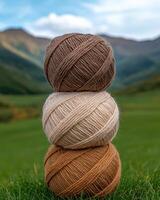Three balls of yarn in autumnal colors stacked on grass with mountains in the background photo