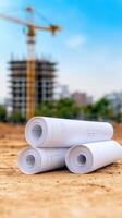 Architecture Blueprints with Rolled Papers on Construction Site Background Featuring Crane and Building Under Blue Sky photo