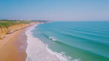 Aerial View of Ocean Waves Rolling and Crashing on Rocky Coastline with Clear Blue Sky and Pristine Sandy Beach in Summer Landscape, Capturing Idyllic Nature and Scenic Tranquil Coastal Beauty photo