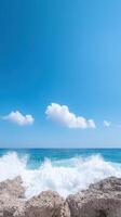 Slow Motion Waves Crashing on Huge Stones Under Clear Blue Sky with Fluffy White Clouds in Summer Beach Scene photo