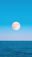 Moon Over Tranquil Sea with Blue Skies in Vertical Format, 916 Aspect Ratio, Ideal for Serene Nature Backgrounds and Celestial Themes. photo