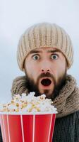 Surprised Man in Winter Attire Holding Bucket of Popcorn Outdoors in Snowy Weather for Seasonal Lifestyle Theme photo