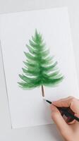 Hand painting a green watercolor Christmas tree on white textured paper photo