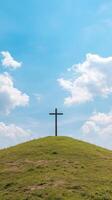 Black cross standing on a grassy hilltop under a bright blue sky with fluffy white clouds in the background. photo