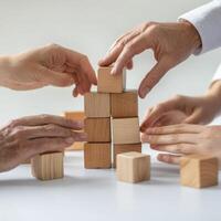 Hands stack wooden blocks together in a collaborative building activity at a light workspace during daytime photo