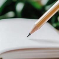 Close-up of a sharpened pencil poised above a blank notebook with plant background in a creative workspace setting photo