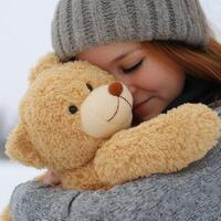 Young girl hugging a teddy bear while enjoying a snowy day outdoors near a serene winter landscape photo