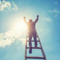 Climbing towards the sun, a person ascends a ladder under a bright blue sky and fluffy clouds photo