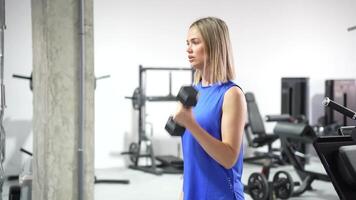 At a contemporary gym, a youthful lady is focused on performing bicep curls with dumbbells video