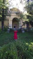 A woman in a red dress takes a photo of an abandoned mansion, nestled in a dense forest. The image highlights the eerie beauty of decaying architecture, with sunlight filtering through the trees. video