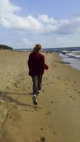 A back view of a girl running on a sandy beach, her hair flowing in the wind near the sea. Footprints in the sand and the distant shore enhance the feeling of freedom and dynamic motion. video