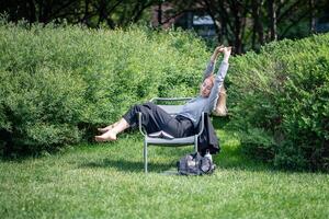 Woman resting, relaxing and stretching while lying on lounge chair in summer green park or garden. photo
