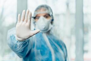 Concept of coronavirus quarantine, global covid-19 epidemic. Treatment of infection. Medic in hazrat protective suit show hands gesture for stop corona virus outbreak photo