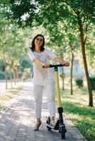 Joyful adorable senior woman using a scooter while riding in the park. Modern woman, a new generation. Healthy cheerful senior retired lady. Concept of Age Inclusivity and ecological transport photo