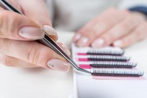 Eyelash Extension Procedure. Close-up of a master at work artificial eyelash extensions material. Hands of the master taking lashes from the set photo
