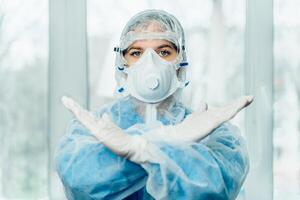 Concept of coronavirus quarantine, global covid-19 epidemic. Treatment of infection. Medic in hazrat protective suit show hands gesture for stop corona virus outbreak photo