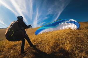 paraglider prepares for a paragliding flight or has already completed it and landed, standing on a hill in the grass, surrounded by a vibrant autumn landscape photo