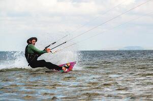 Professional kiter makes the difficult trick on a beautiful background. Kitesurfing Kiteboarding action photos man among waves quickly goes