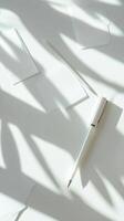 A pen is sitting on a white surface with a shadow of the pen on the surface photo