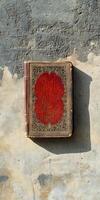 A red book with gold embossing sits on a wall photo