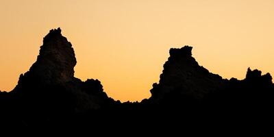 Two large rocks are silhouetted against a sunset photo