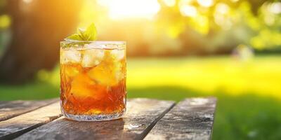 A glass of iced tea sits on a wooden table in a park photo