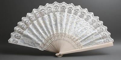 A white lace fan is displayed on a grey background. The fan is open and has a lace design on it photo