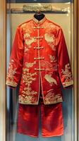 A man in a red Chinese outfit with gold embroidery. The outfit is displayed in a glass case photo