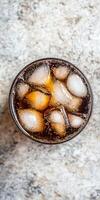 A glass of soda with ice cubes in it. The ice cubes are in the middle of the glass, and the soda is brown in color photo