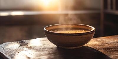 A rustic bowl of steaming soup sits on a wooden table, capturing the essence of comfort and warmth. The soft sunlight creates an inviting scene, perfect for a cozy meal. photo