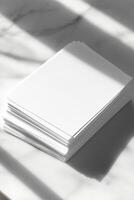 A stack of blank white paper sheets on a marble surface, illuminated by sunlight, casting soft shadows for a minimalist aesthetic. photo
