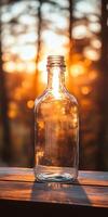 Sunlit Glass Bottle on Wooden Table with Warm Sunset Background in Tranquil Outdoor Setting photo
