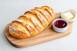 recién horneado de masa fermentada un pan servido en un de madera tablero con mantequilla y mermelada en pequeño platos, Perfecto para desayuno o un bocadillo foto