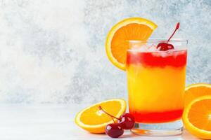 Vibrant tequila sunrise cocktail with layers of orange and red garnished with cherry and orange slice against a modern backdrop photo