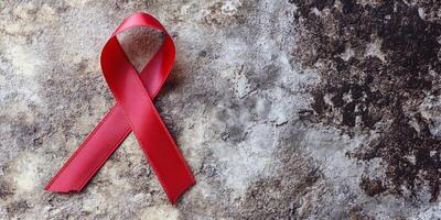 Red ribbon symbolizing awareness and support for HIV AIDS displayed on rustic wall photo
