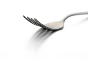 Elegant silver fork resting on a reflective surface with soft lighting creating delicate shadows photo