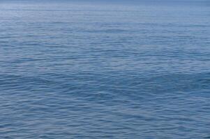 Calm waves gently lap against the shore at a tranquil seaside location in midday sunlight photo