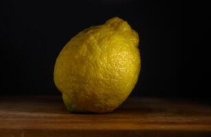 Bright yellow lemon resting on a wooden surface with soft shadows in the background under warm lighting photo